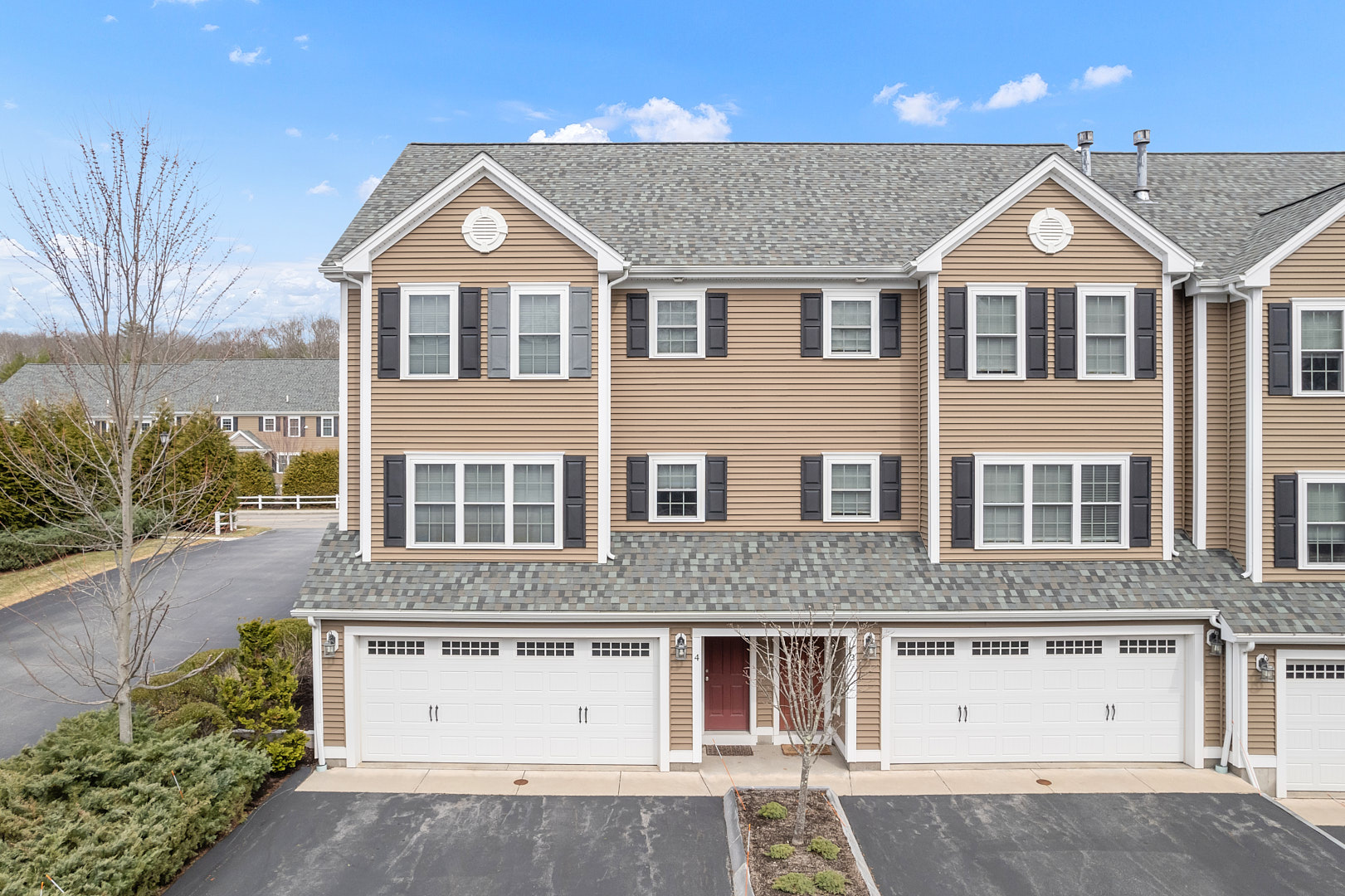 Three-story residential building featuring beige siding and multiple garages in front.