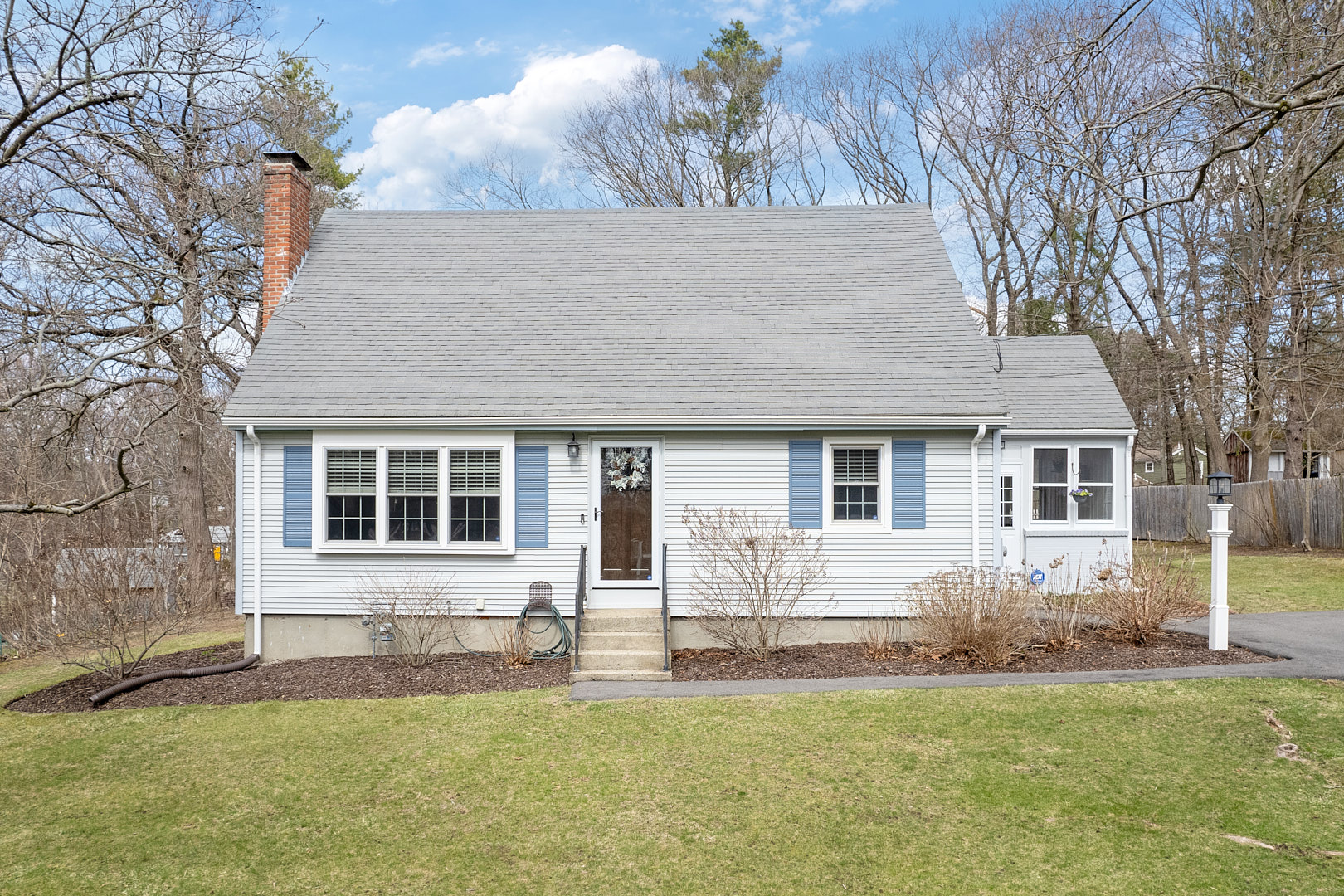 Single-story blue house with a gray roof and front yard, featuring a chimney and white shutters.