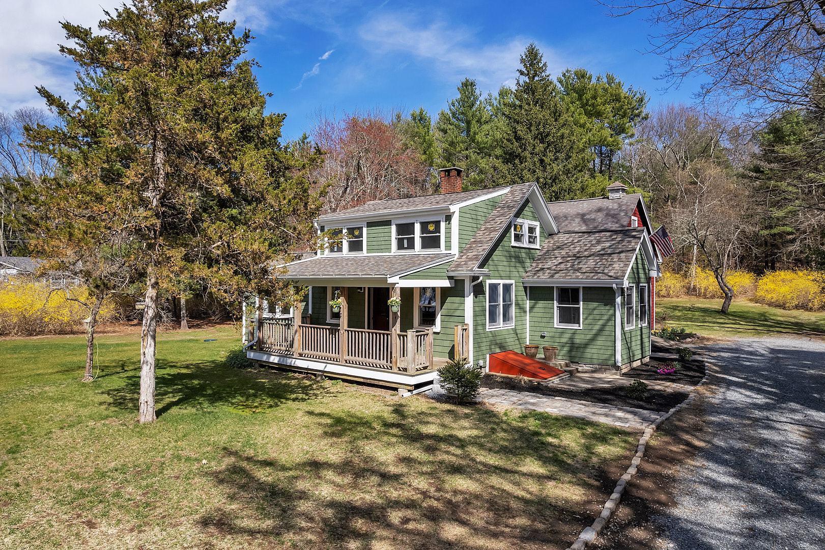 Two-story green house with a porch and a gravel driveway in front.